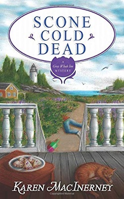 View from a white-railed porch overlooking the ocean and a lighthouse. On the porch, a marmalade cat is napping and there's a table with a plate of scones. On the path leading to the ocean lies a body partially concealed in foliage.